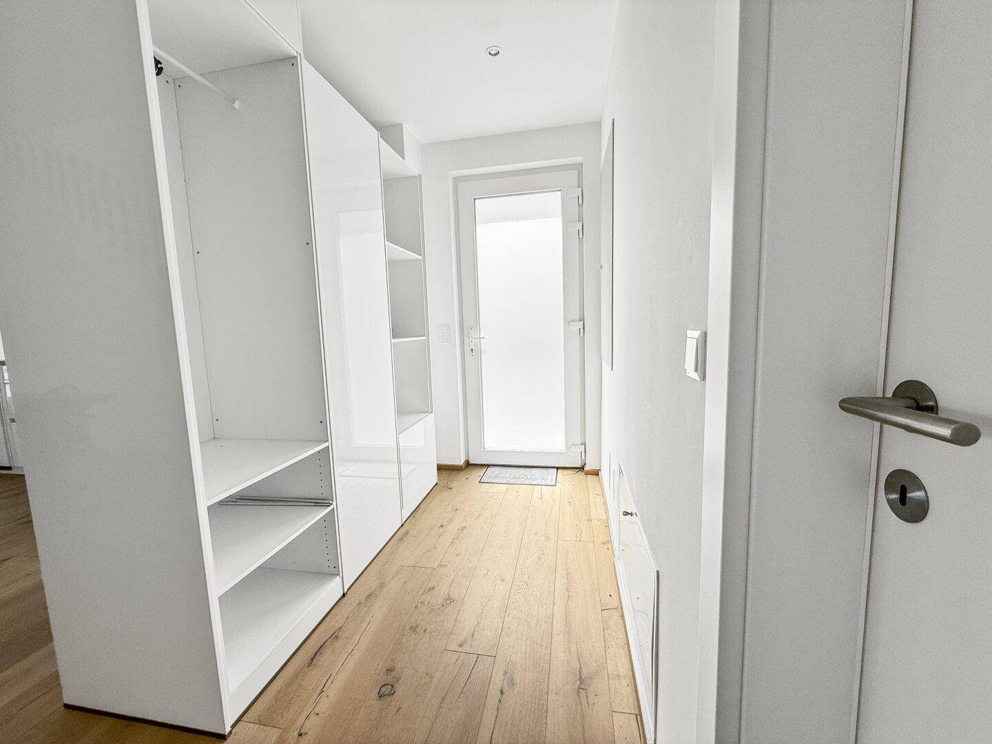 Eingangsbereich mit Holzboden, weißen Einbauschränken und heller Eingangstür.