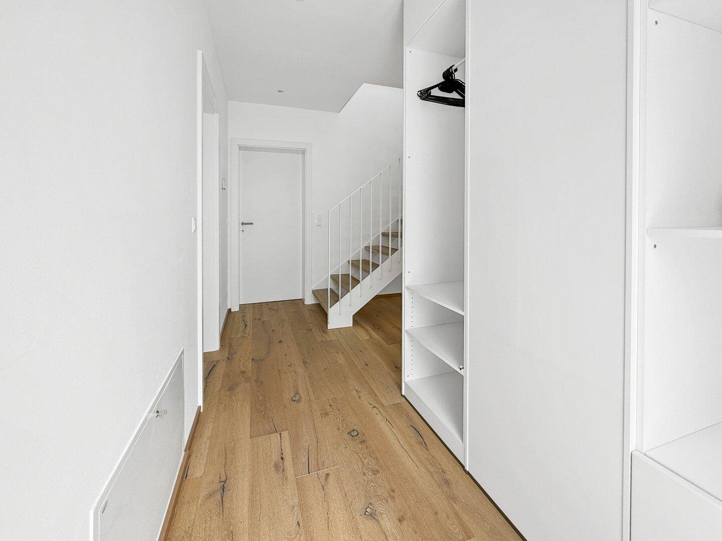 Heller Flur mit Holzboden und integrierten weißen Einbauschränken.