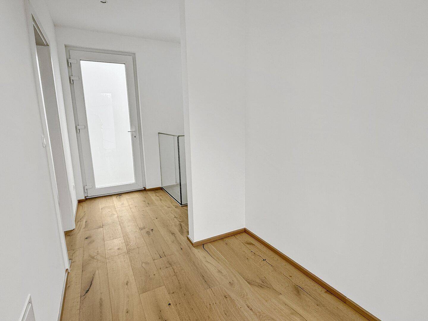 Heller Flur mit Holzboden und weißer Wandgestaltung.
