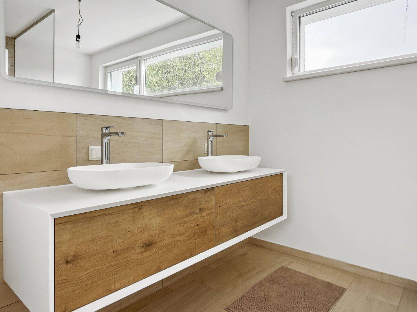 Modernes Badezimmer mit Doppelwaschbecken, Holzelementen und großem Spiegel.