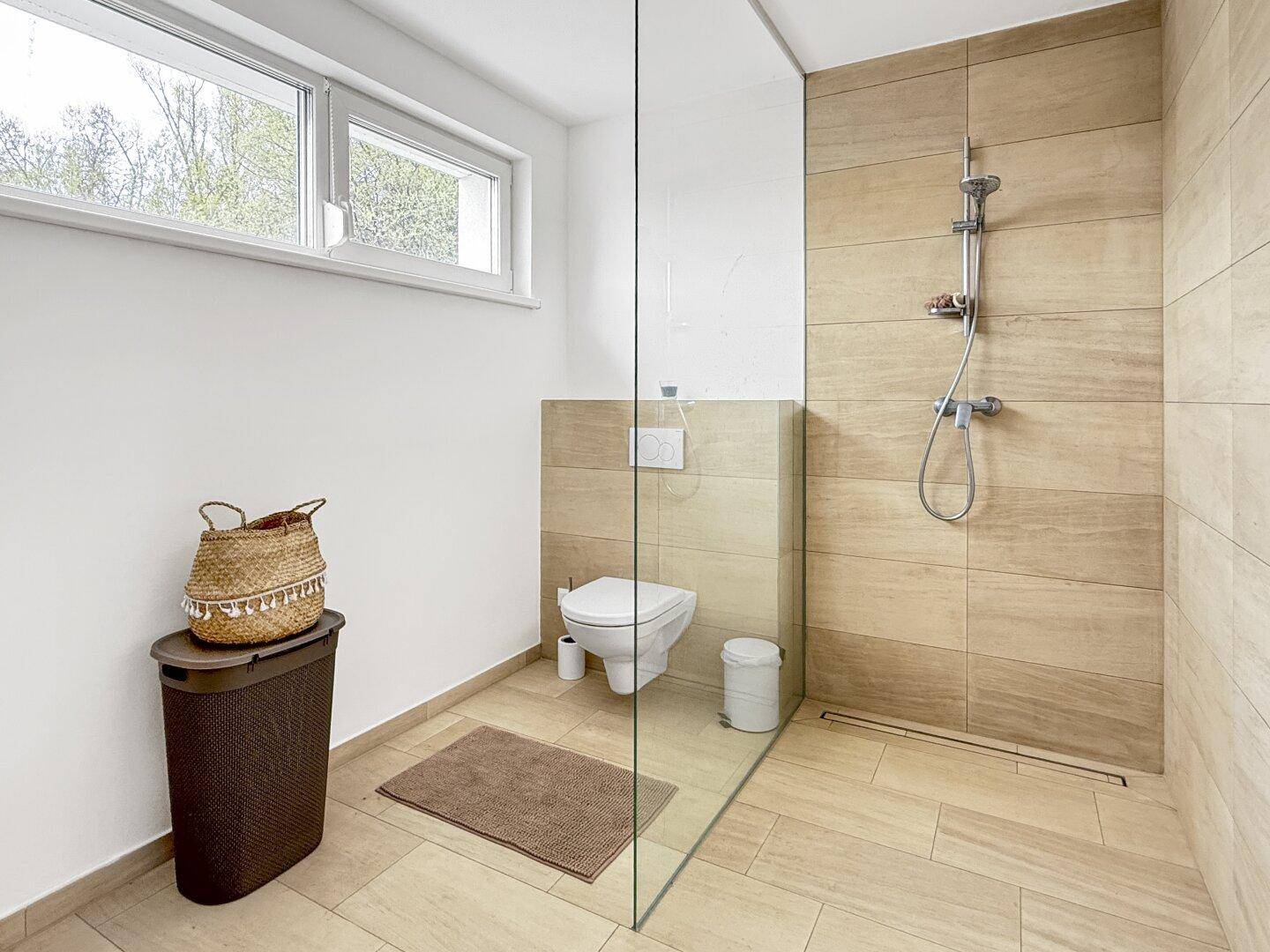 Helles Badezimmer mit begehbarer Dusche, WC und Fenster für natürliche Belüftung.