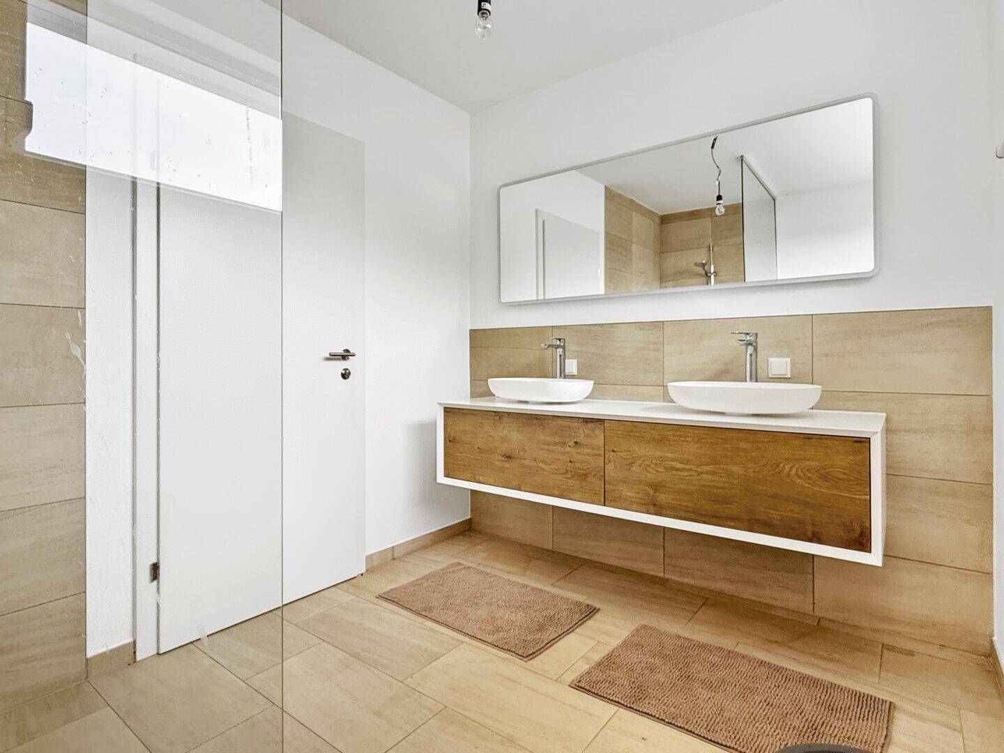 Modernes Badezimmer mit Doppelwaschbecken, Holzelementen und großem Spiegel.