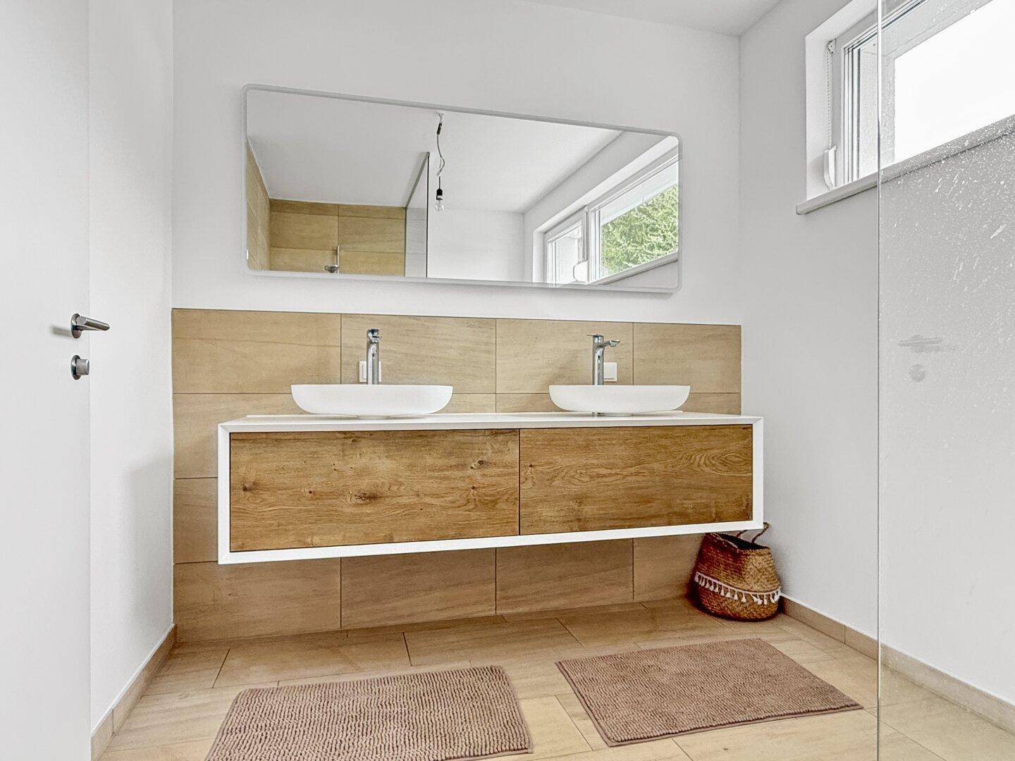 Helles Badezimmer mit Doppelwaschbecken, Holzelementen und großem Spiegel.
