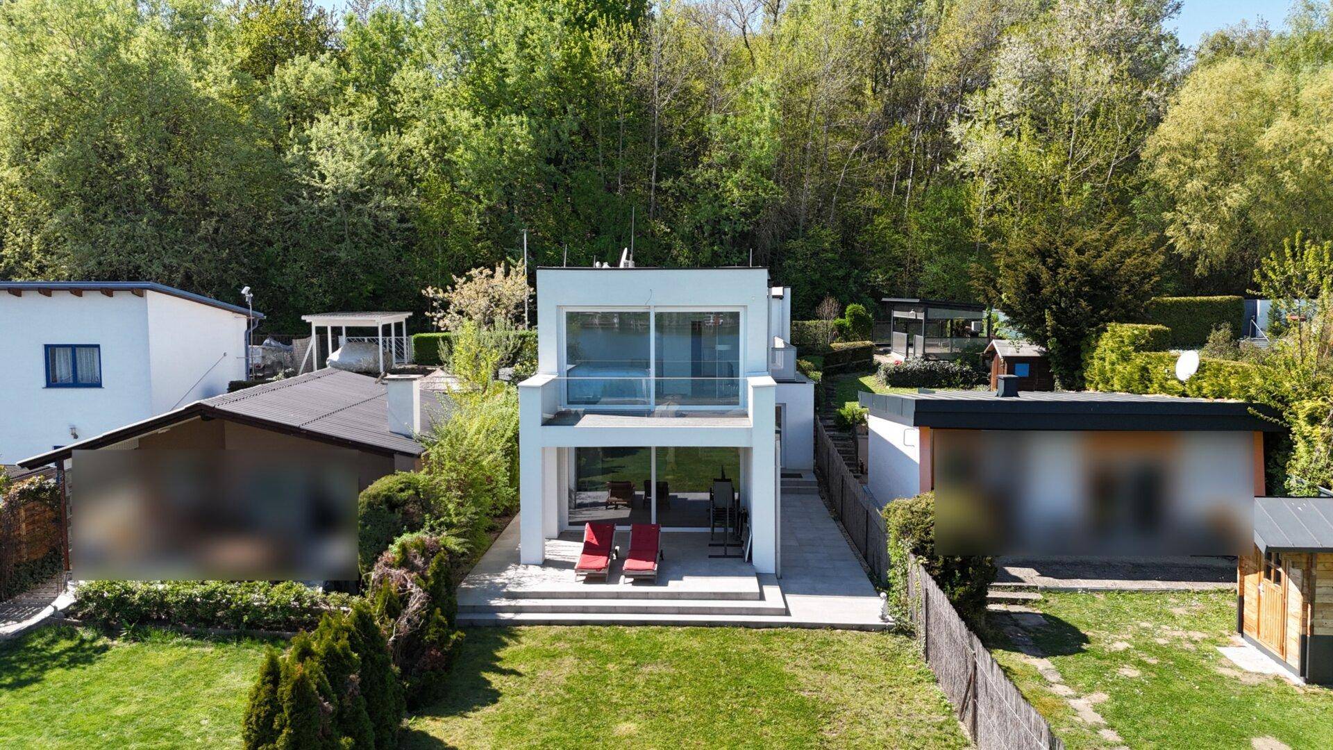 Luftaufnahme des modernen Hauses mit Garten und Terrasse am See.
