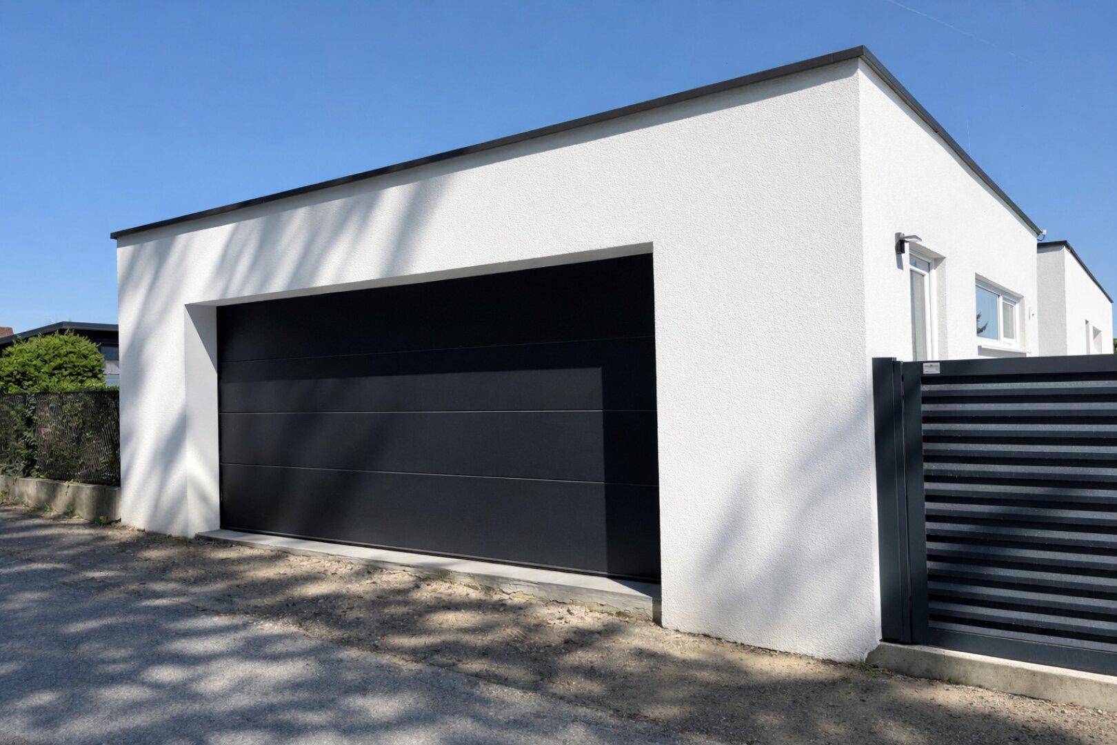Moderne Garage mit schwarzem Garagentor und weißer Fassade.