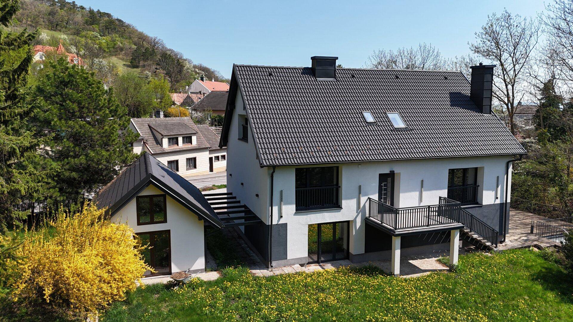 Rückansicht des Hauses mit Garten, Balkon und Blick auf die umliegende Hügellandschaft.