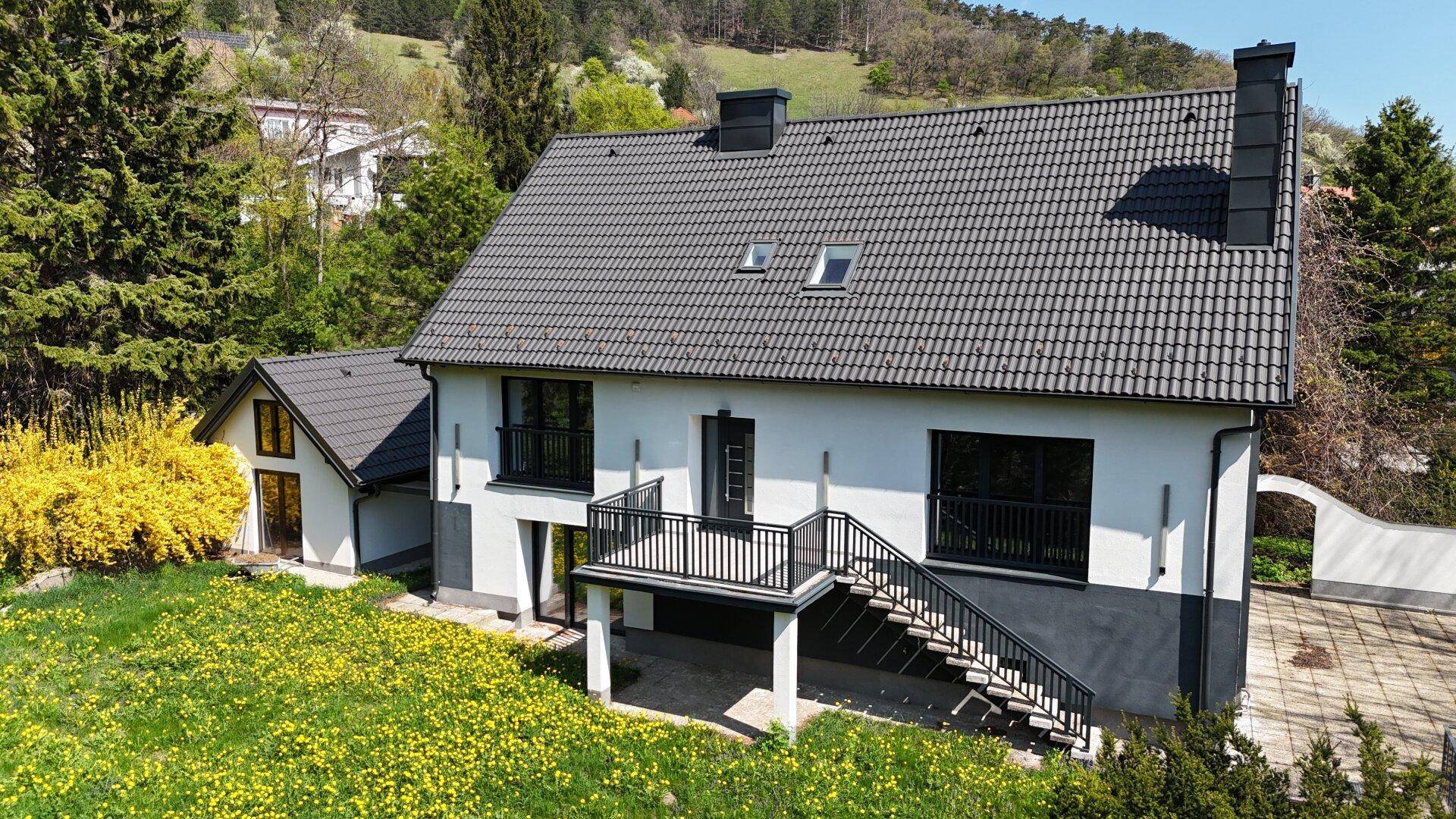 Rückansicht des Hauses mit Garten, Balkon und Blick auf die umliegende Hügellandschaft.
