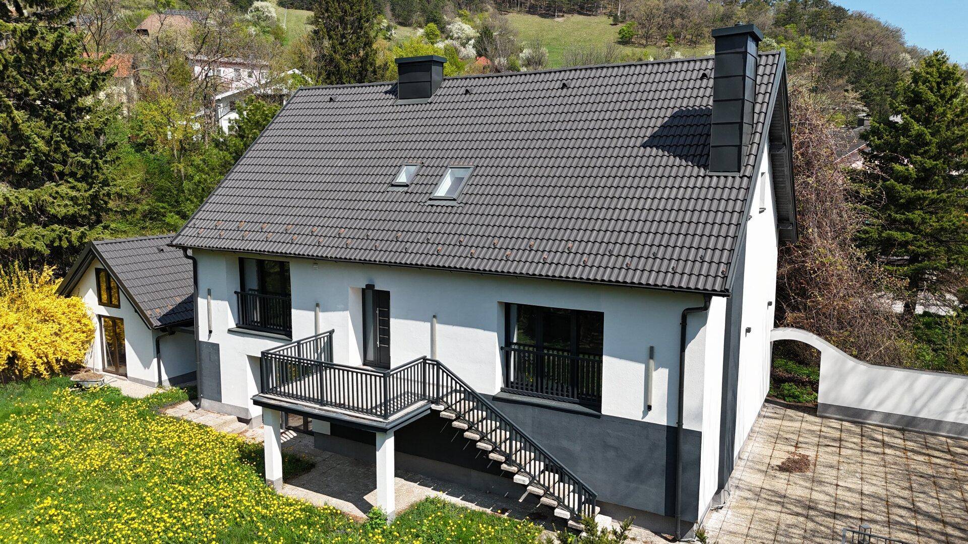 Rückansicht des Hauses mit Garten, Balkon und Blick auf die umliegende Hügellandschaft.