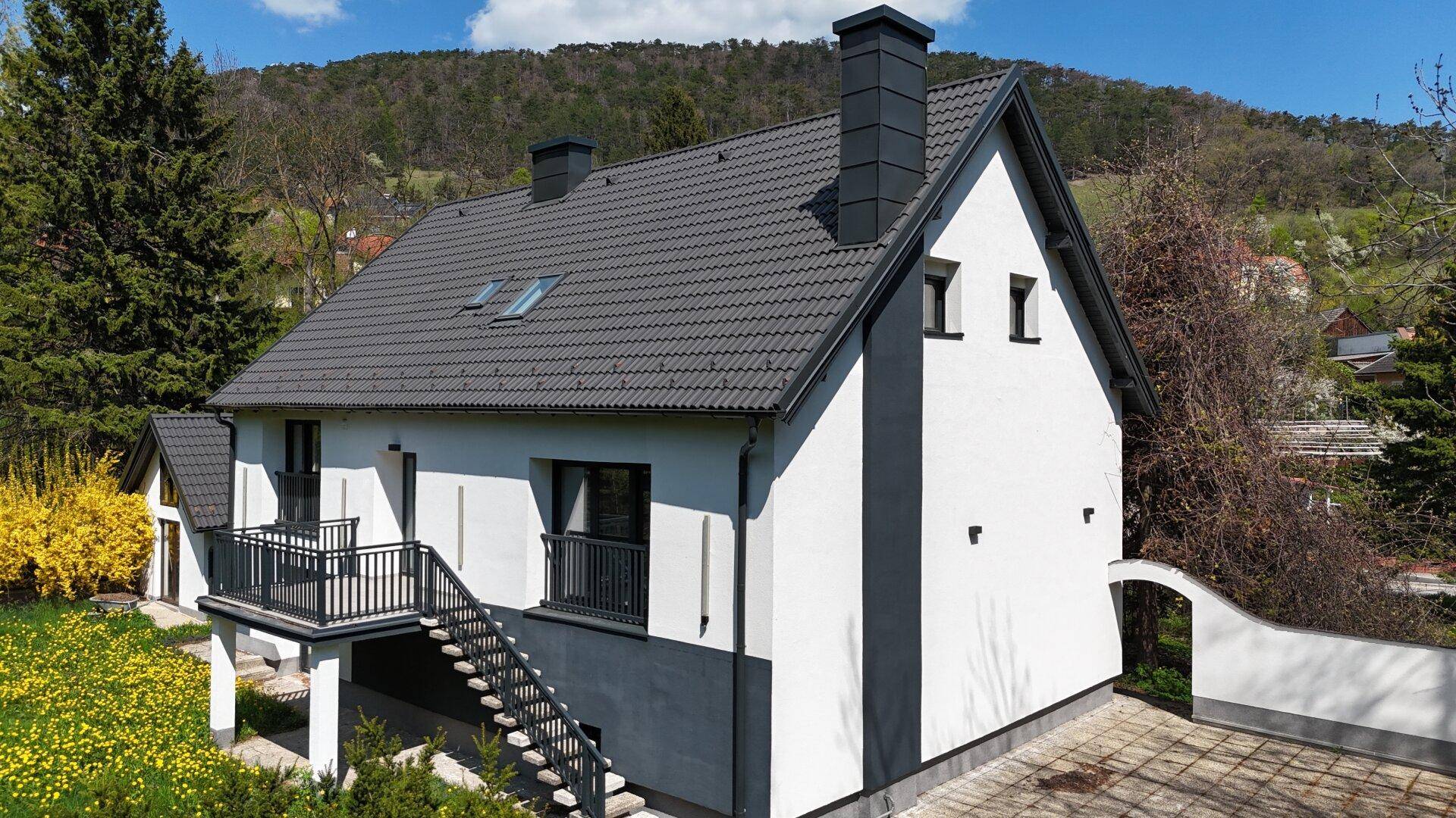 Seitenansicht des modernen Hauses mit Balkon, Außentreppe und Garten.