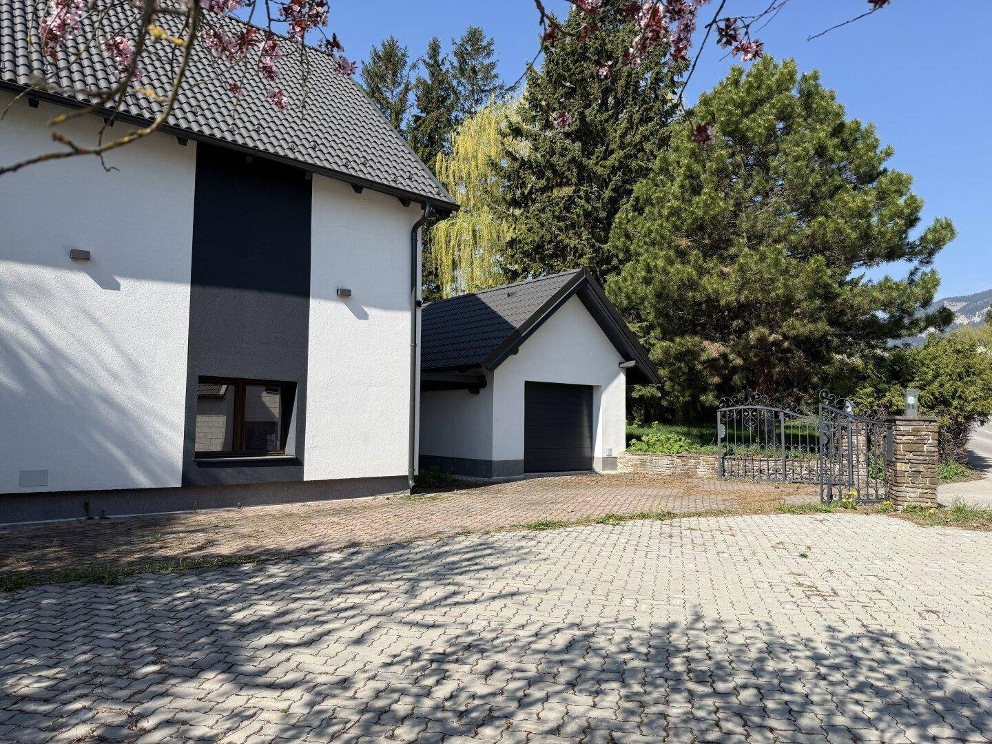 Seitenansicht des Hauses mit Garage, gepflasterter Fläche und Blick auf die Umgebung.