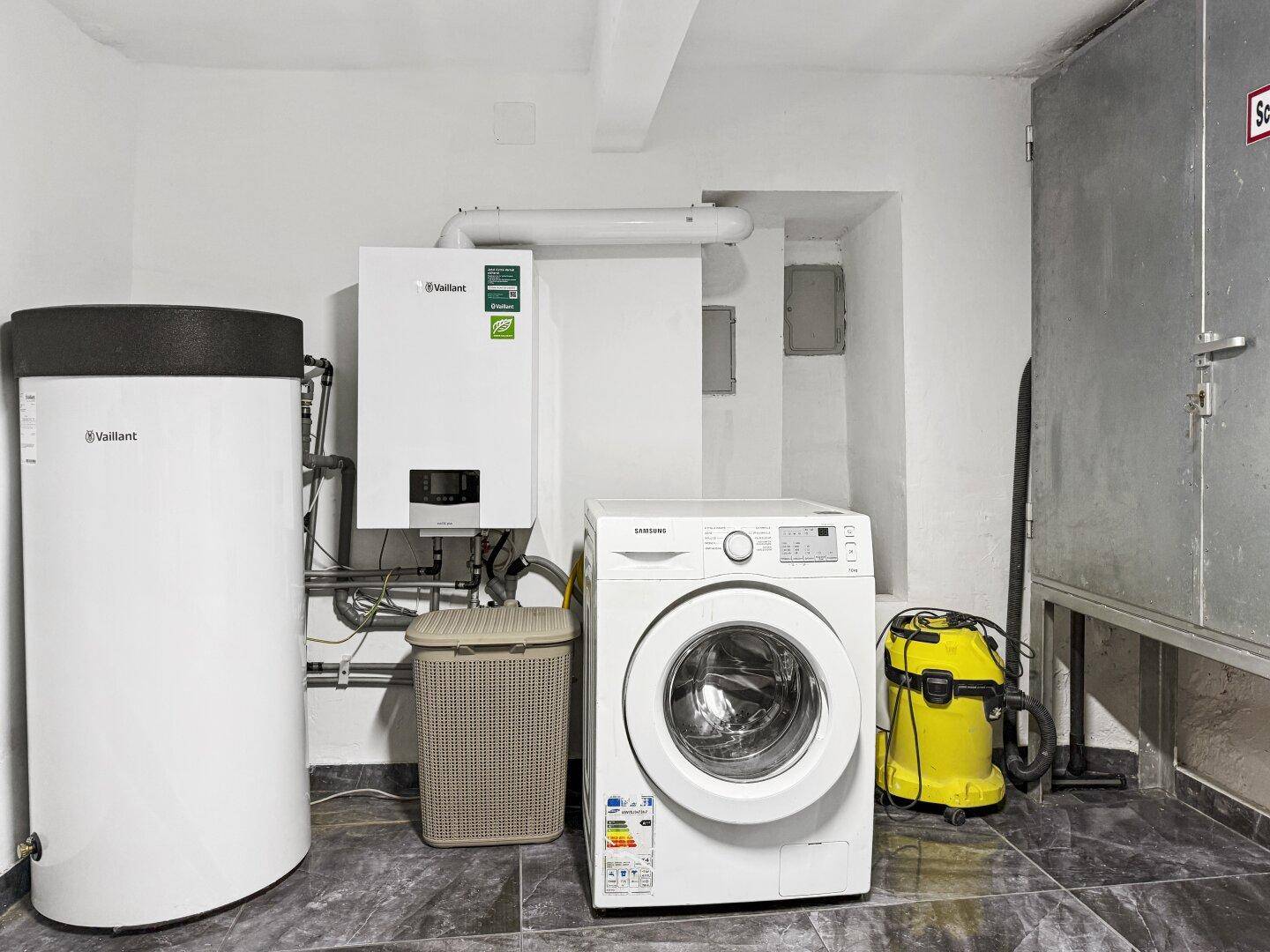 Hauswirtschaftsraum mit Waschmaschine, Warmwasserspeicher und Heizungsanlage.