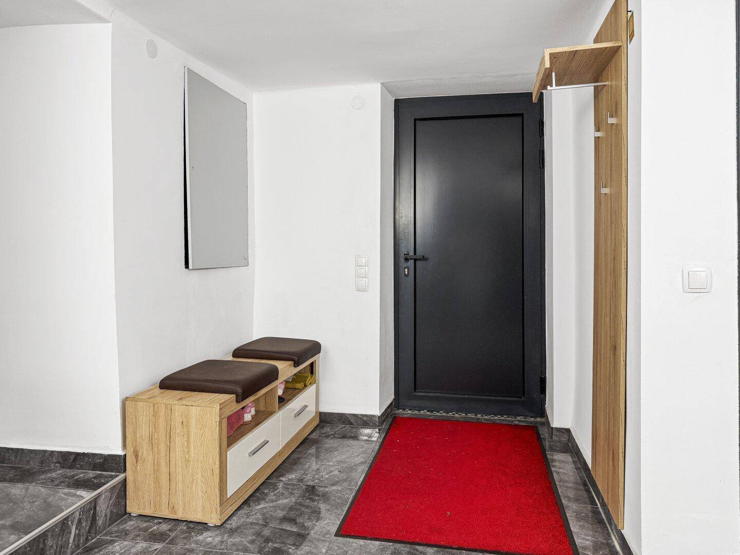 Eingangsbereich mit dunklem Fliesenboden, Garderobe und moderner Haustür.