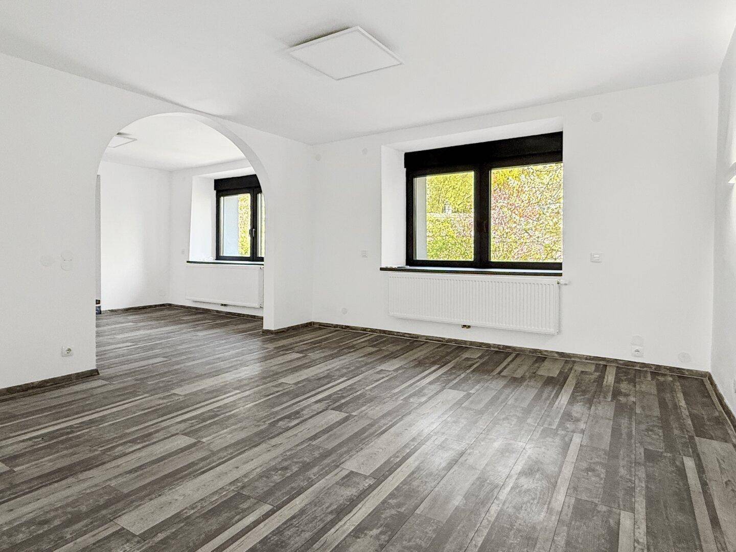 Offener Wohnbereich mit Holzbodenoptik und elegantem Rundbogen.
