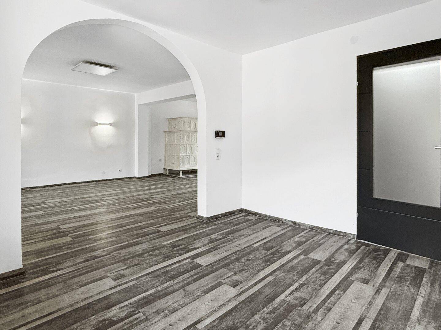 Geräumiger Wohnbereich mit Holzbodenoptik, Rundbogen und moderner Tür.