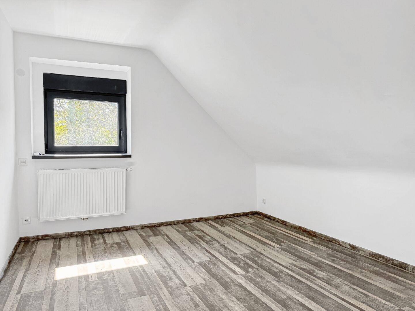 Helles Schlafzimmer im Dachgeschoss mit Holzbodenoptik und Fenster.