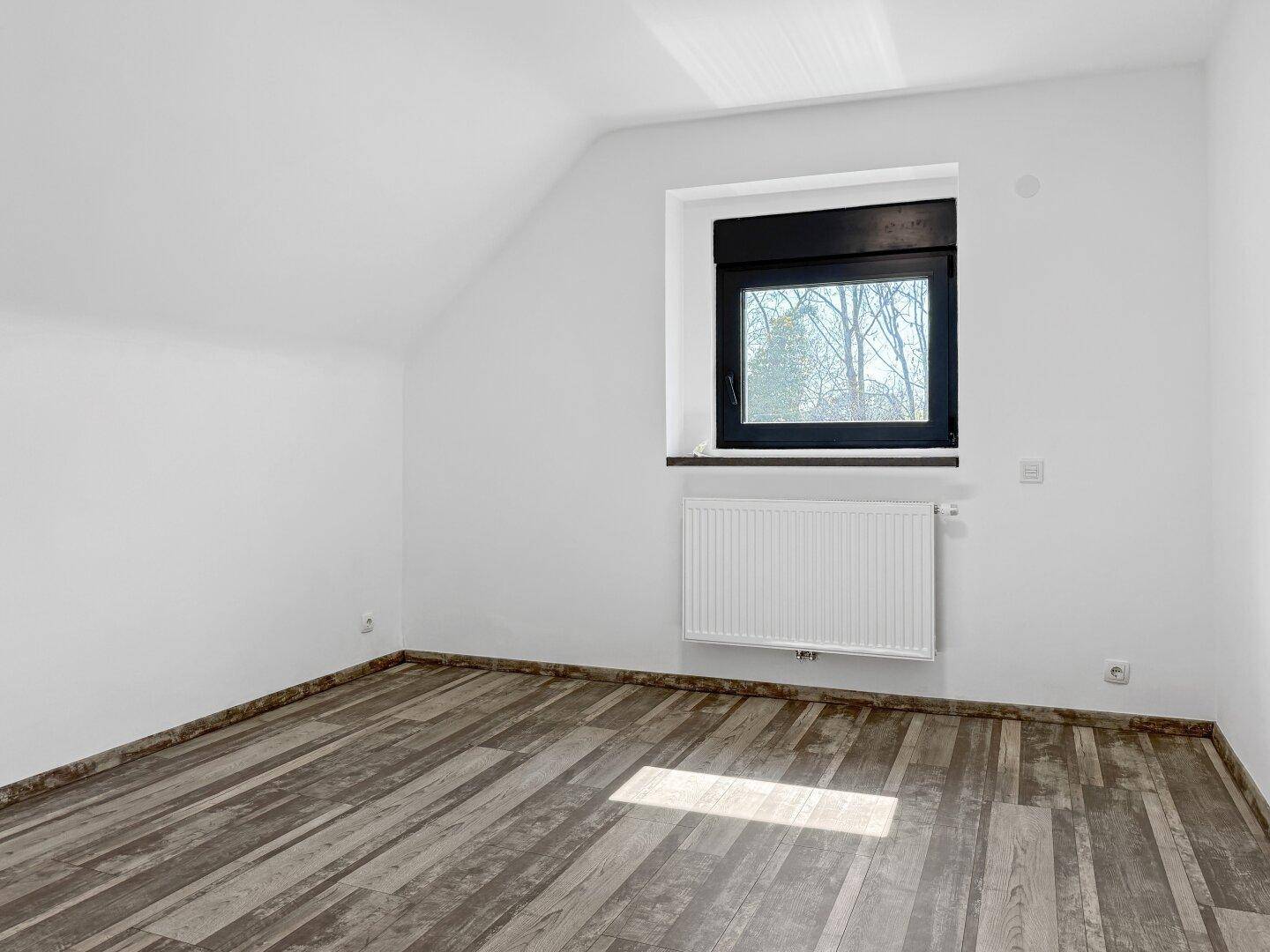 Helles Schlafzimmer im Dachgeschoss mit Holzbodenoptik und Fenster.