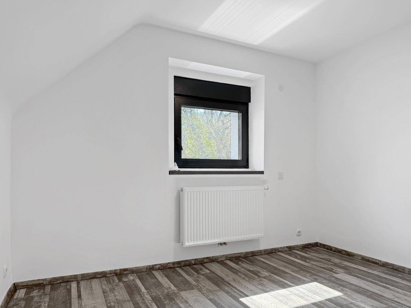 Helles Schlafzimmer im Dachgeschoss mit Holzbodenoptik und Fenster.