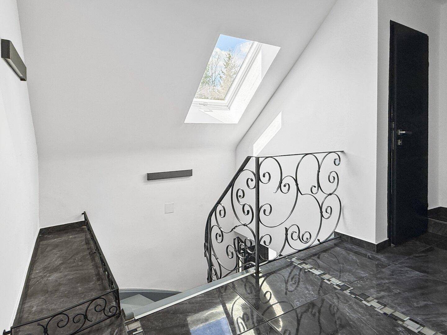 Helles Treppenhaus mit schmiedeeisernem Geländer und Dachfenster für Tageslicht.