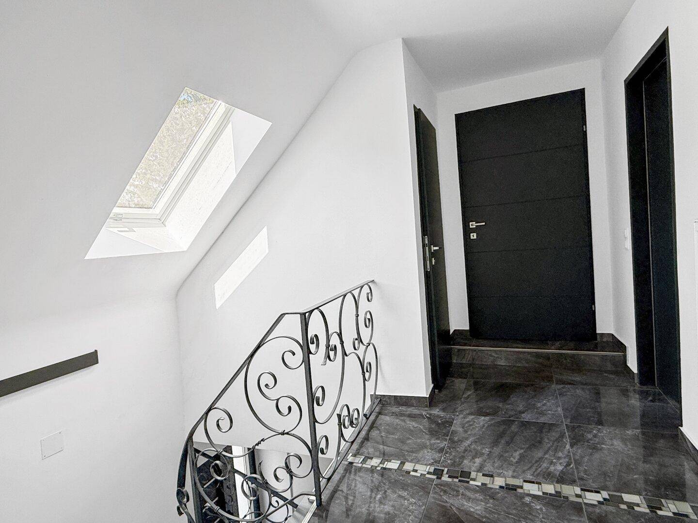 Heller Flur im Dachgeschoss mit Dachfenster und dunklem Fliesenboden.
