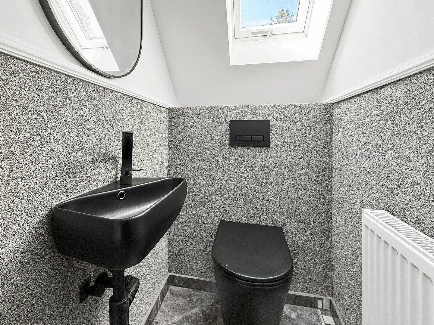 Modernes Gäste-WC im Dachgeschoss mit schwarzem Waschbecken, Toilette und Dachfenster.