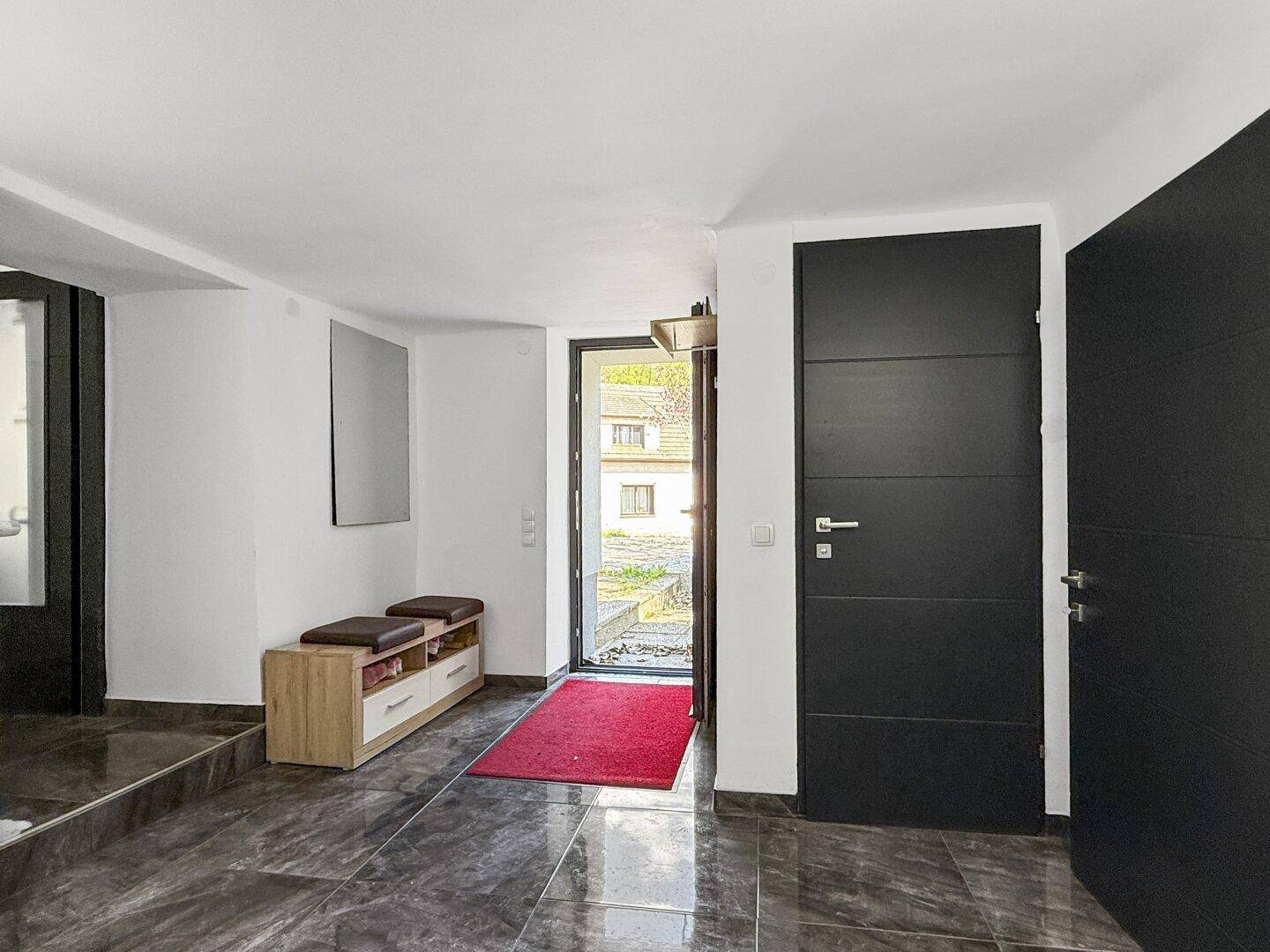 Eingangsbereich mit dunklem Fliesenboden, Garderobe und moderner Haustür.