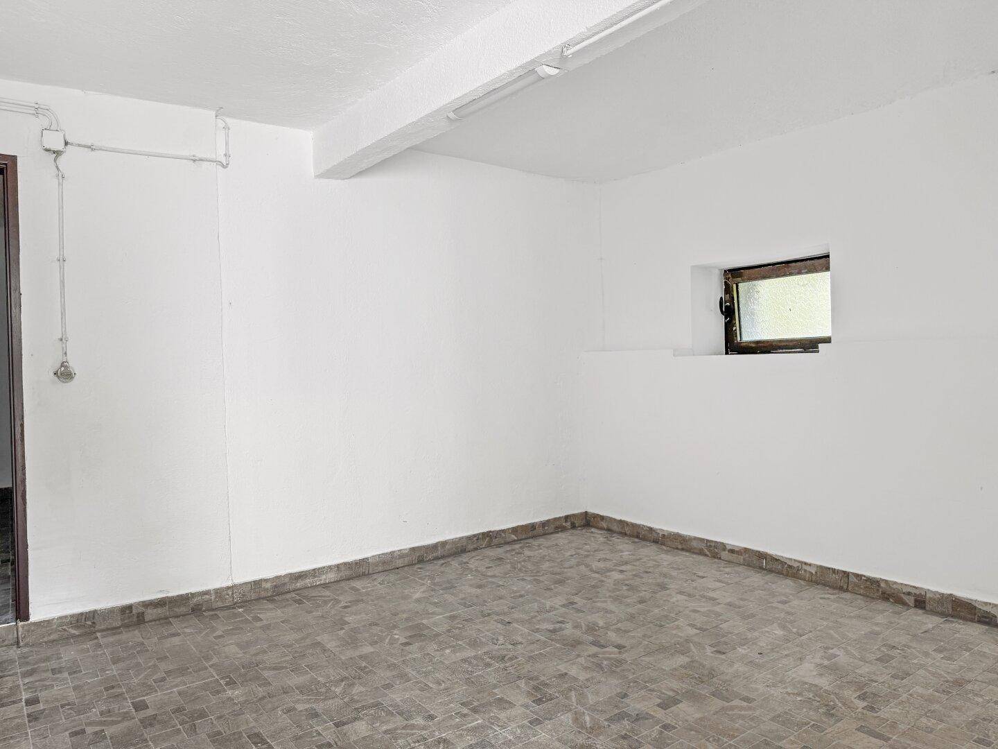 Leerer Kellerraum mit Fliesenboden und kleinem Fenster.