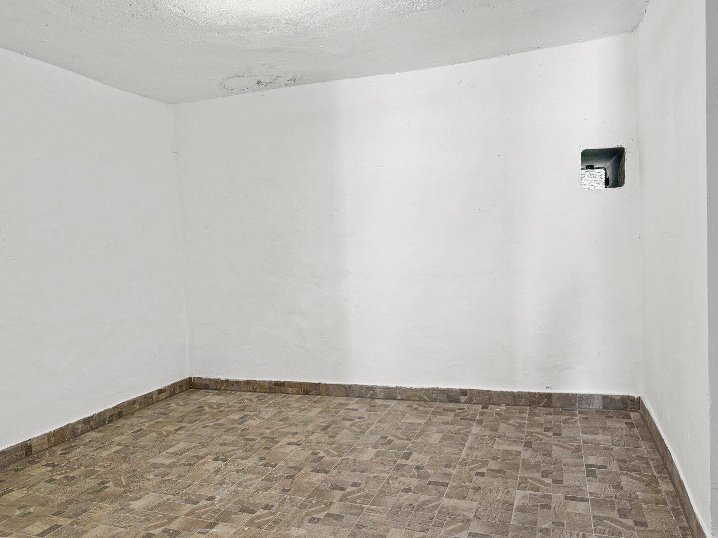 Leerer Kellerraum mit Fliesenboden und weiß gestrichenen Wänden.