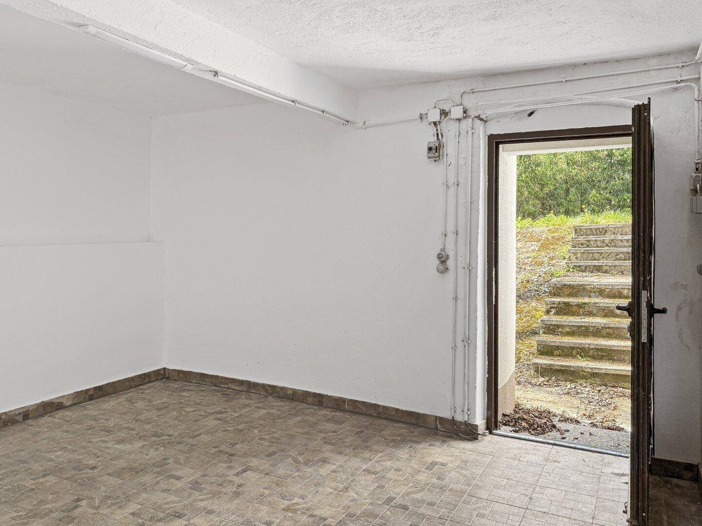 Leerer Kellerraum mit Fliesenboden und Zugang zum Garten.