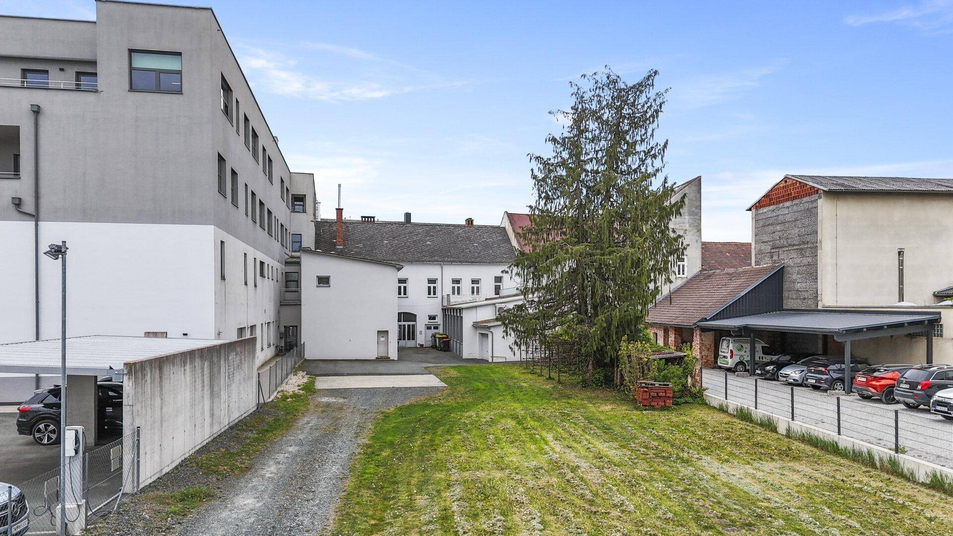 Hinterhofbereich mit Grünfläche, Parkplätzen und angrenzenden Gebäuden unter blauem Himmel.