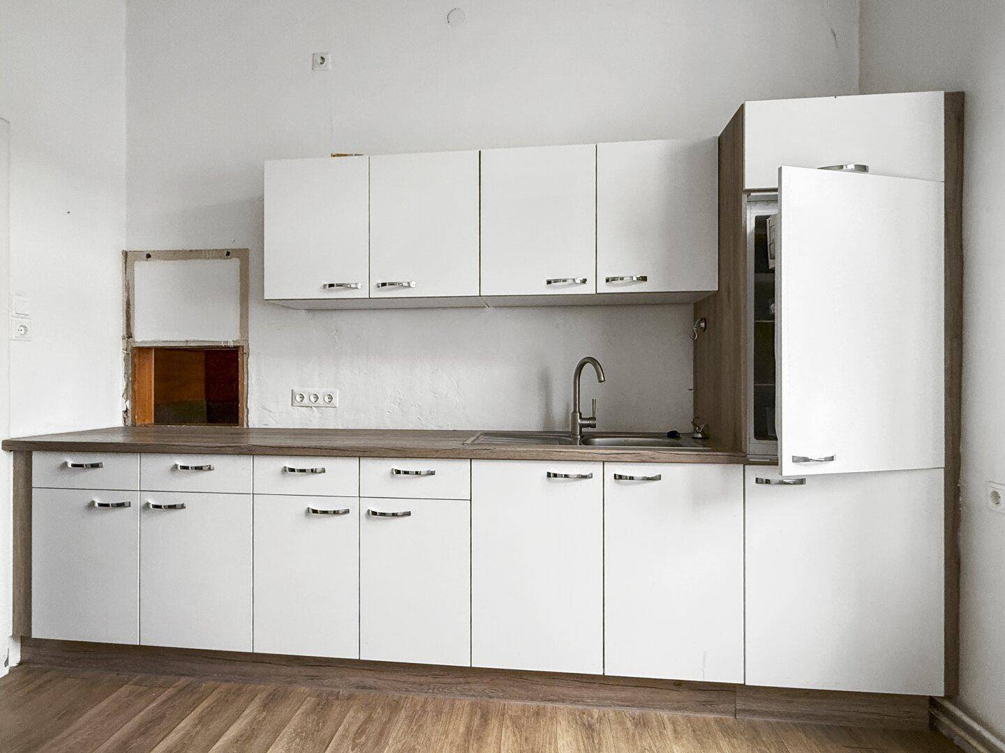 Küchenzeile mit weißen Fronten, Holzoptik-Arbeitsplatte und integriertem Kühlschrank.