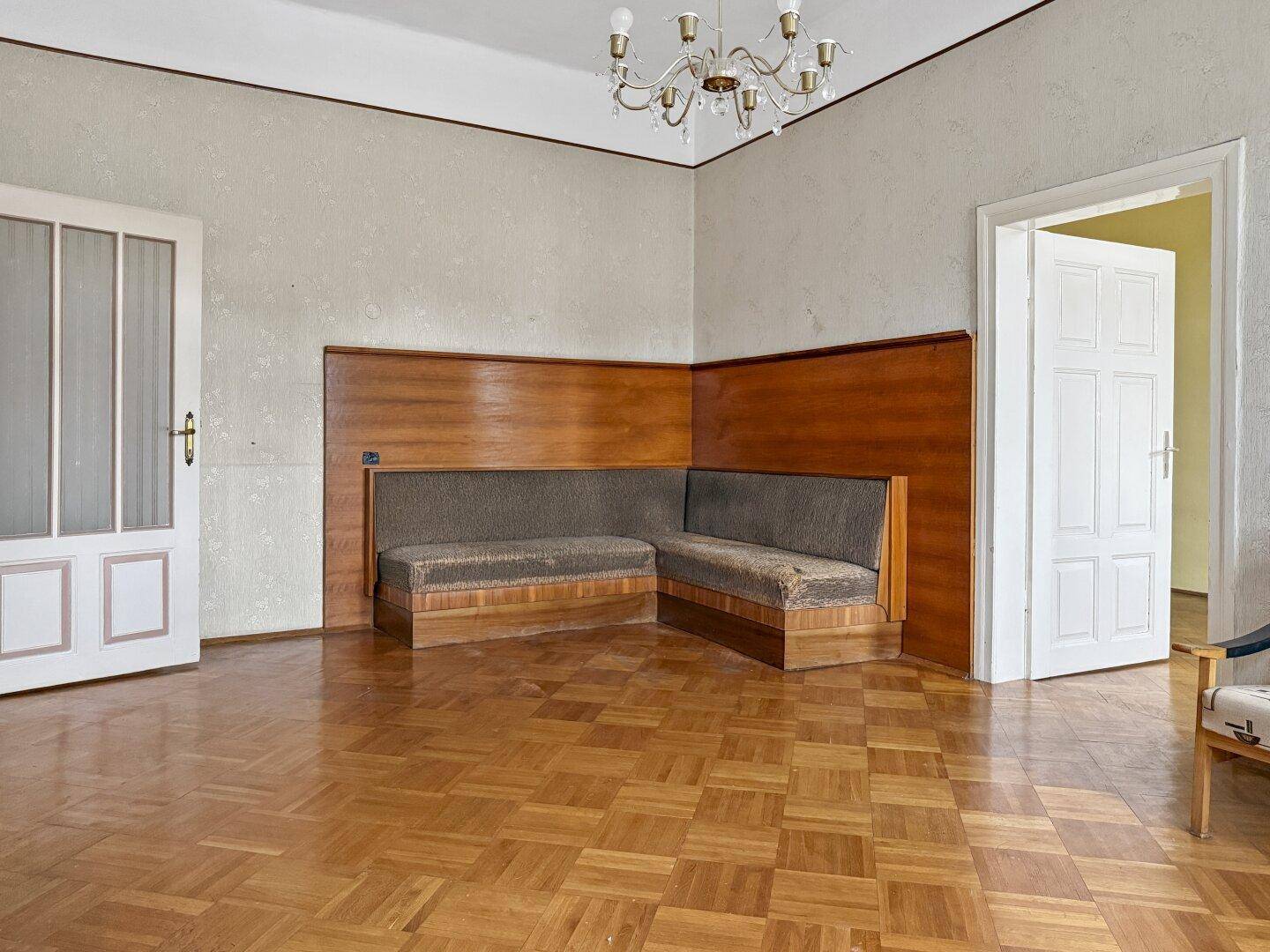 Wohnzimmer mit Parkettboden, Holztäfelung und einer eingebauten Sitzbank, Kronleuchter an der Decke.