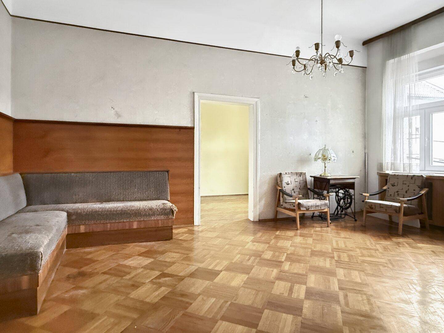 Geräumiges Wohnzimmer mit Parkettboden, Vintage-Möbeln und einem großen Fenster für viel Tageslicht.