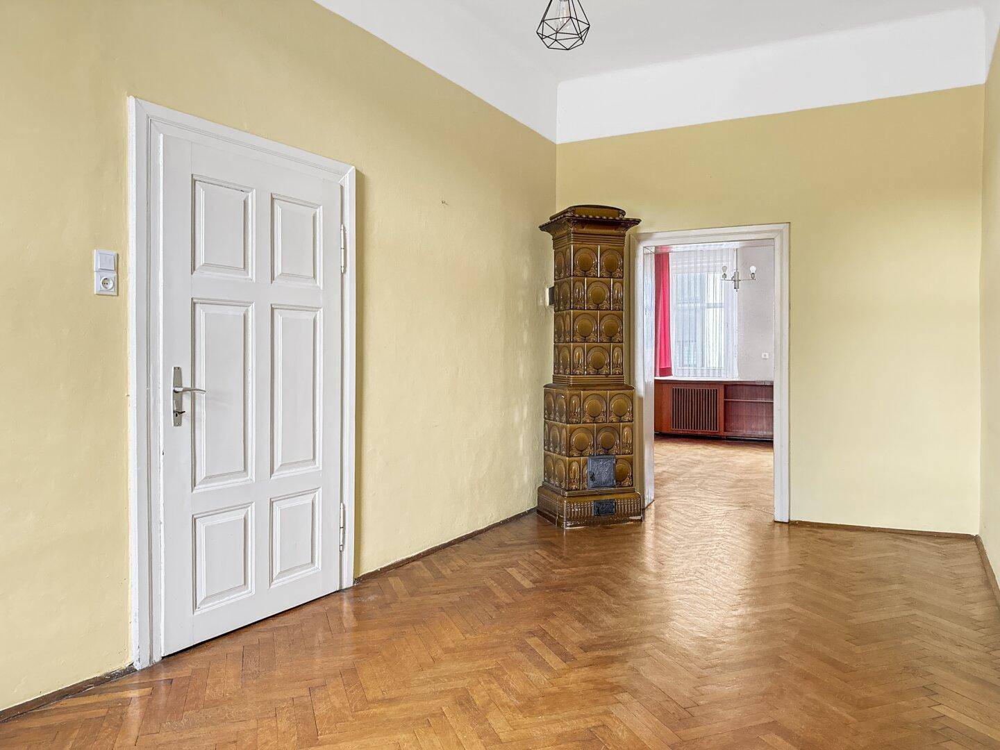 Zimmer mit Parkettboden, gelben Wänden und einem traditionellen Kachelofen als Heizelement.