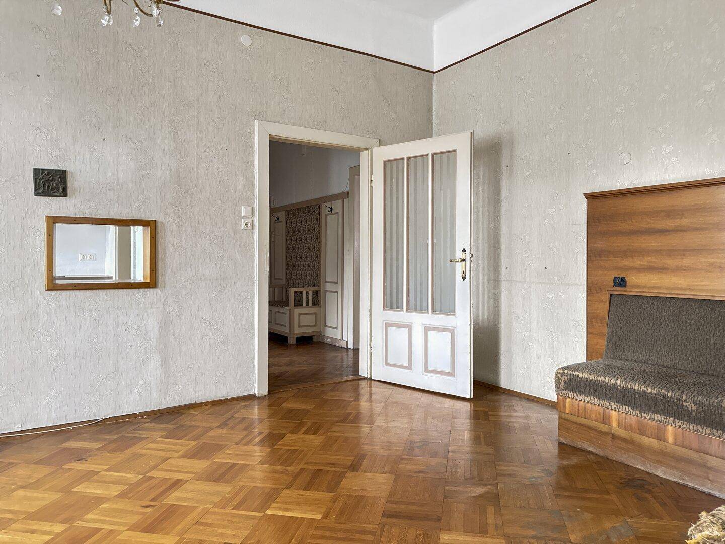 Wohnzimmer mit Parkettboden und Holztäfelung, Blick durch die offene Tür in den Flur.