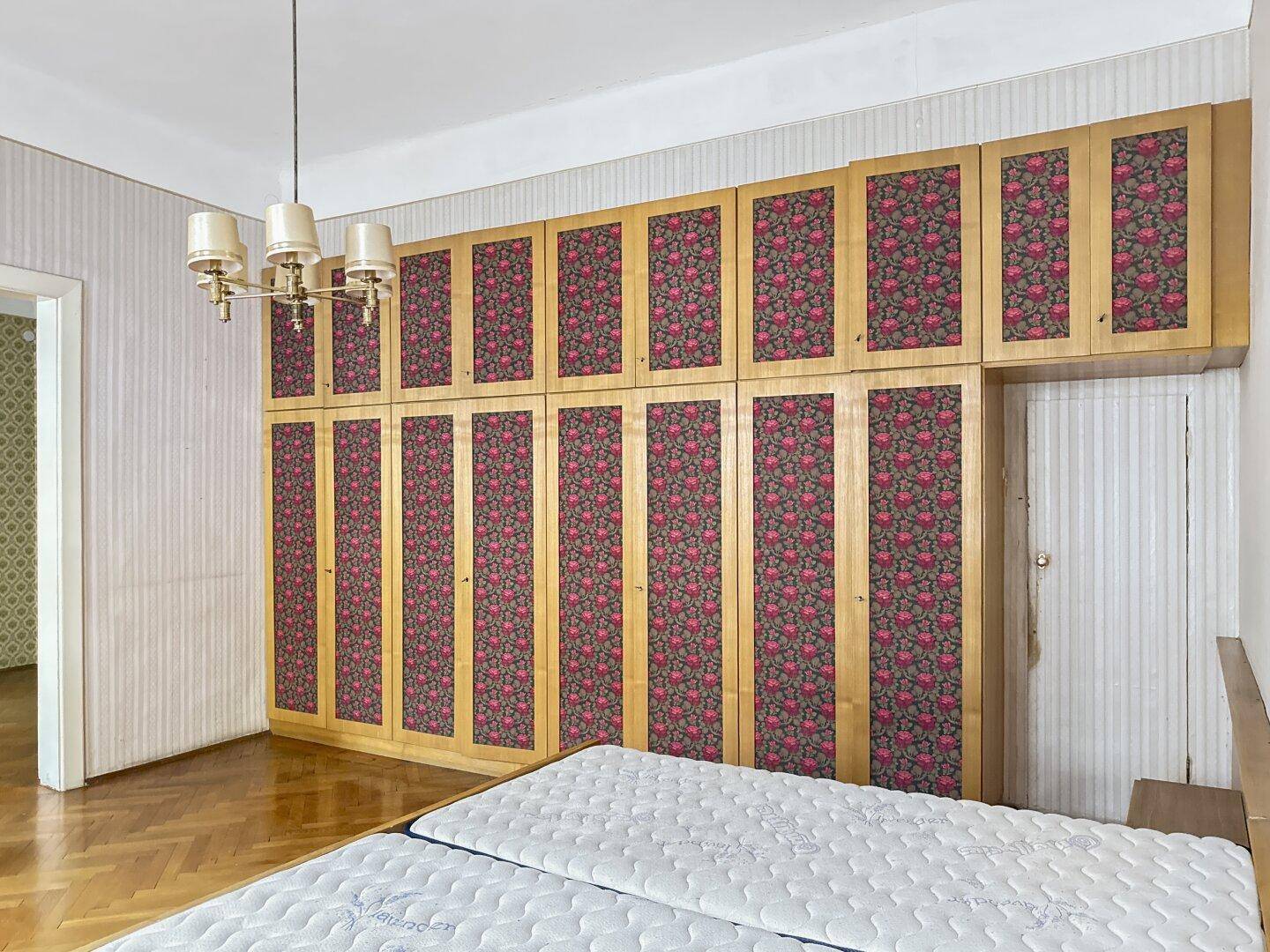 Schlafzimmer mit großen Einbauschränken mit gemusterten Türen und klassischem Fischgrätparkett.