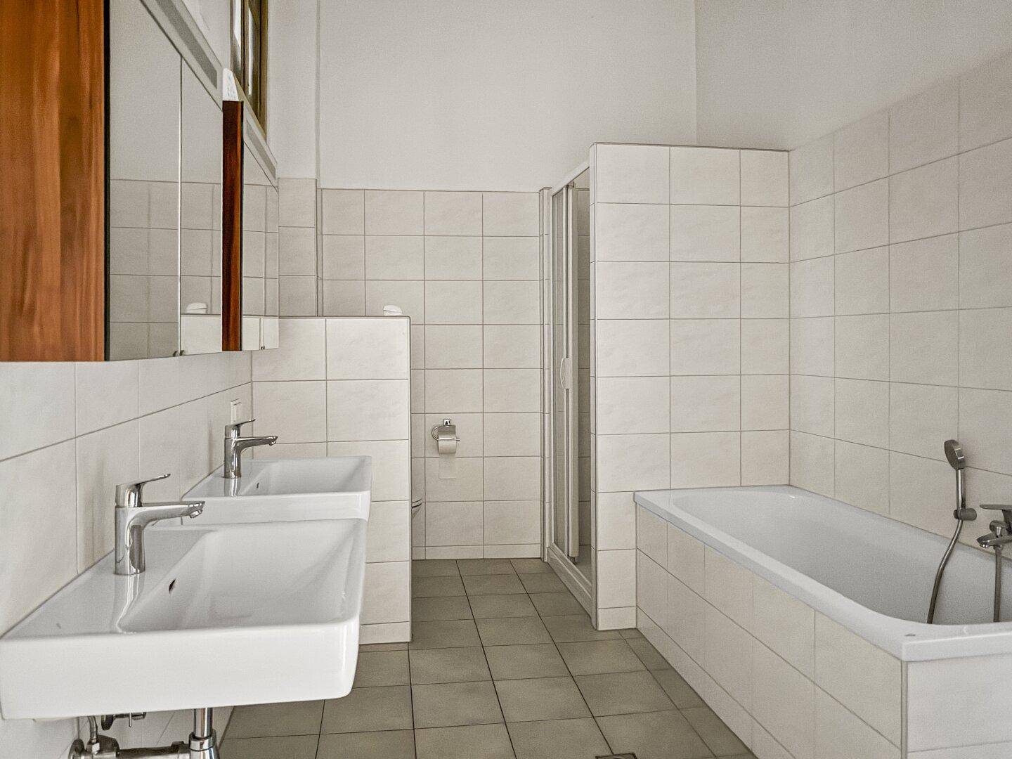 Badezimmer mit zwei Waschbecken, Badewanne und separater Duschkabine, komplett gefliest.