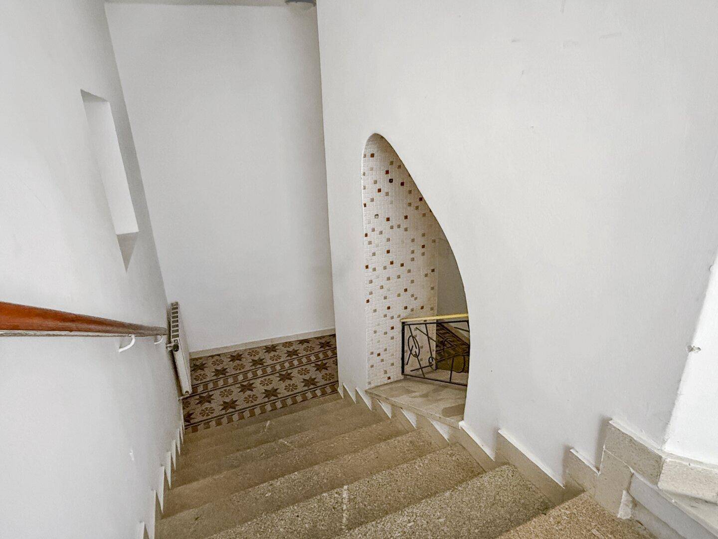 Treppenhaus mit Steinstufen, schlichtem Geländer und dekorativen Fliesen an der Wand.