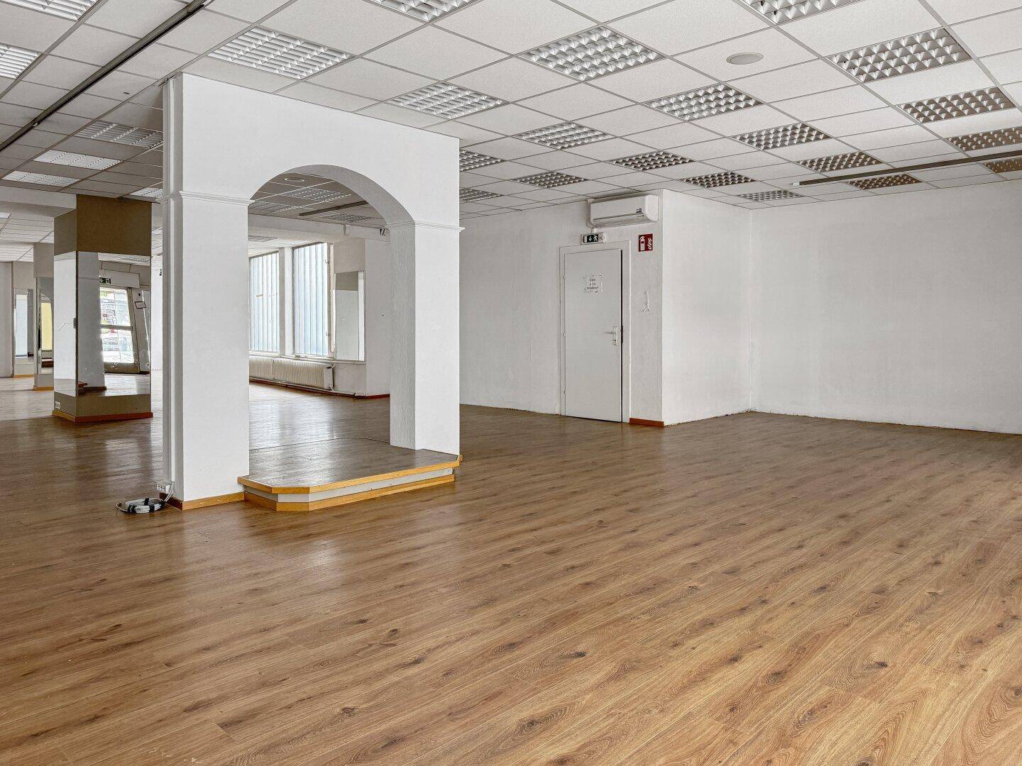 Heller Gewerberaum mit Laminatboden, Rasterdecke und einer weißen Wand mit Tür.