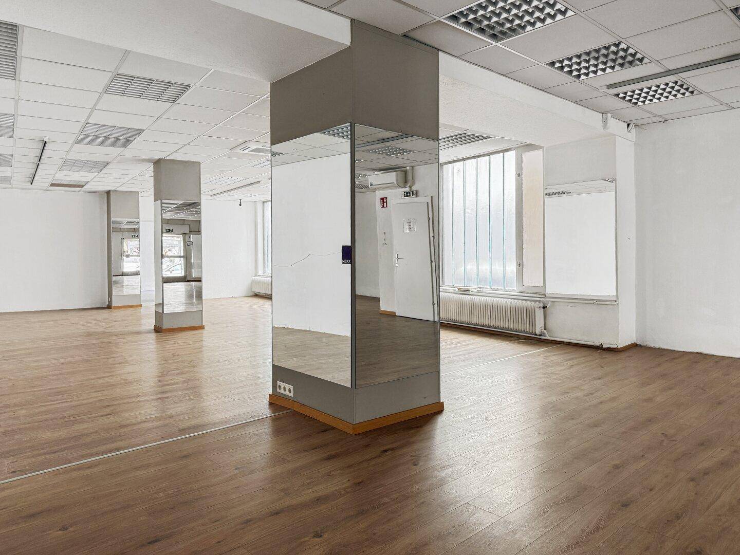 Geräumiger Gewerberaum mit Laminatboden, Rasterdecke und verspiegelten Säulen.
