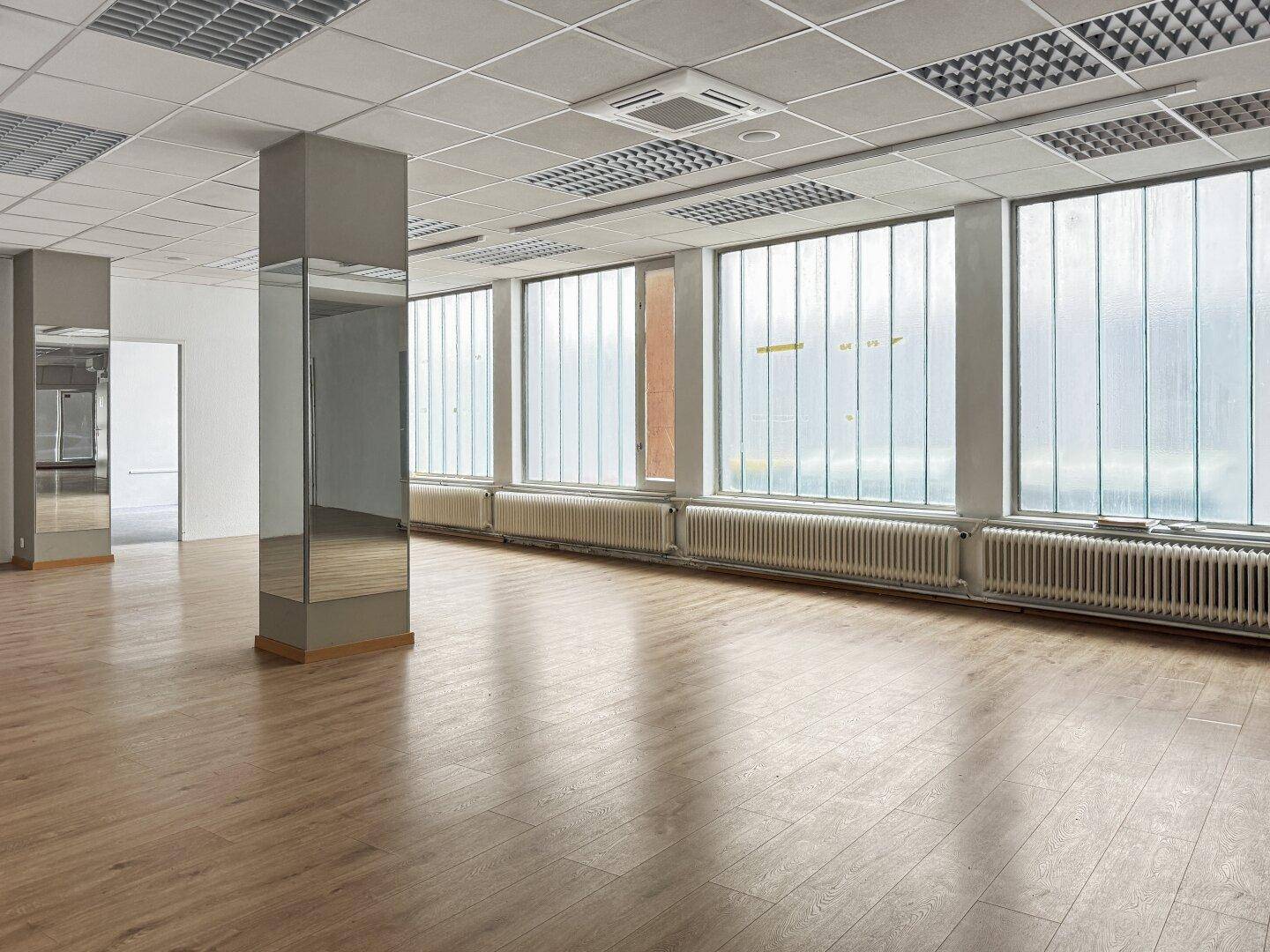 Heller Gewerberaum mit Laminatboden, Rasterdecke und großen Industriefenstern.