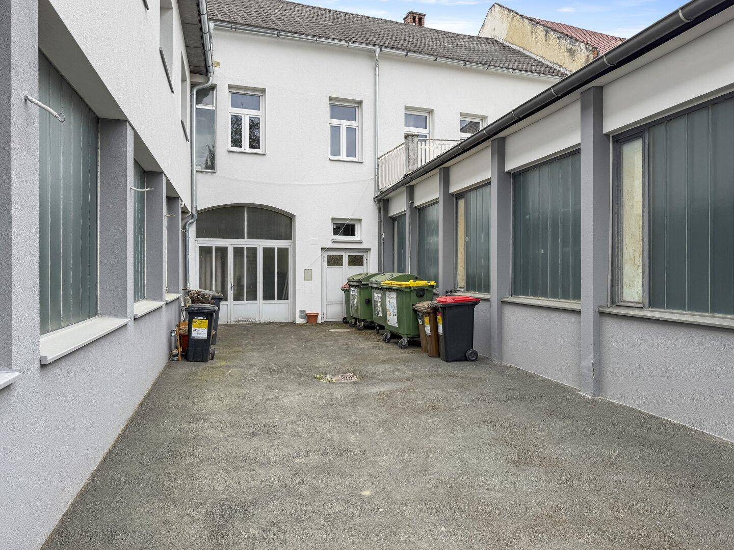 Gepflasterter Innenhof mit Mülltonnen und großen Fenstern der umliegenden Gebäude.