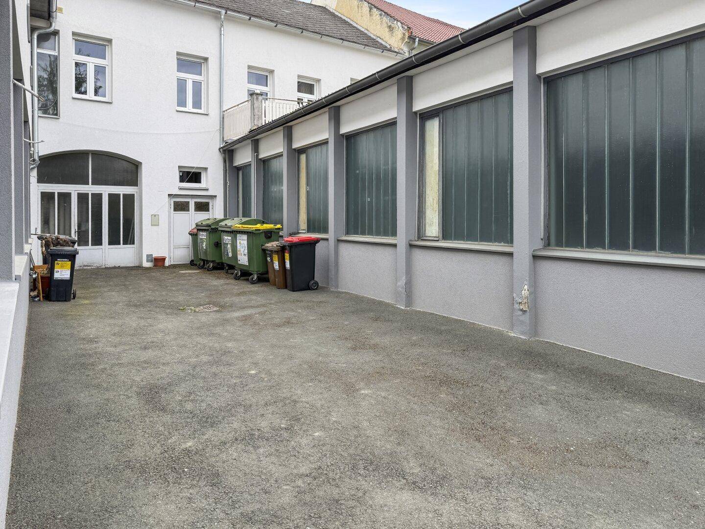 Gepflasterter Innenhof mit Mülltonnen und großen Fenstern der umliegenden Gebäude.