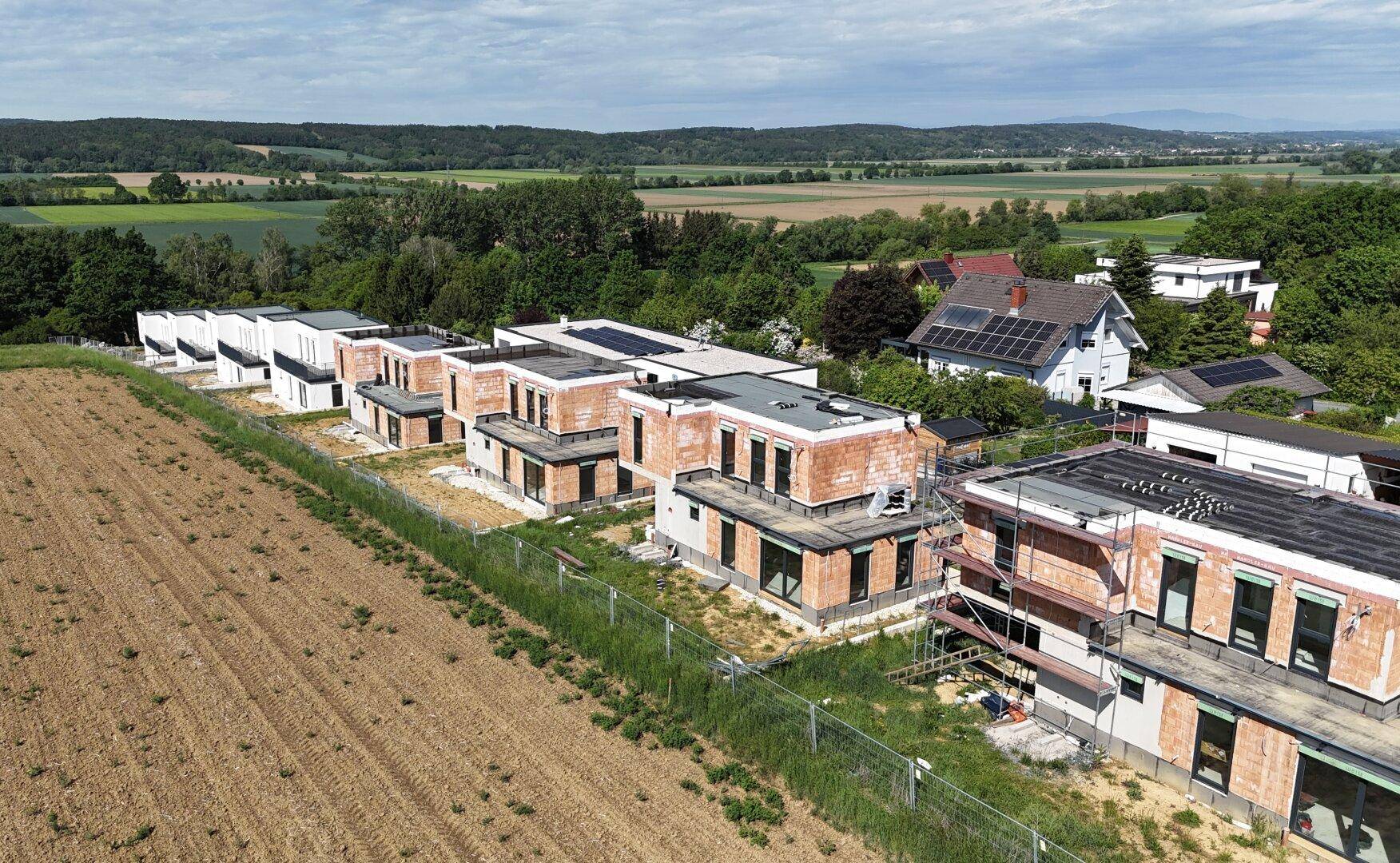 Neubauprojekt mit mehreren Einfamilienhäusern in verschiedenen Bauphasen und ländlichem Ausblick.