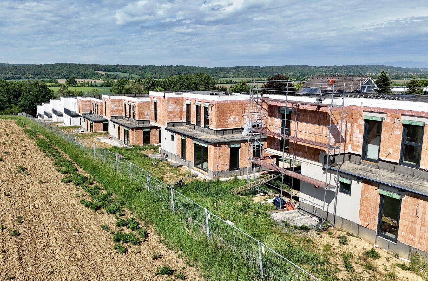 Reihe von Einfamilienhäusern im Bau mit Ziegelfassaden und Gerüsten in ländlicher Umgebung.