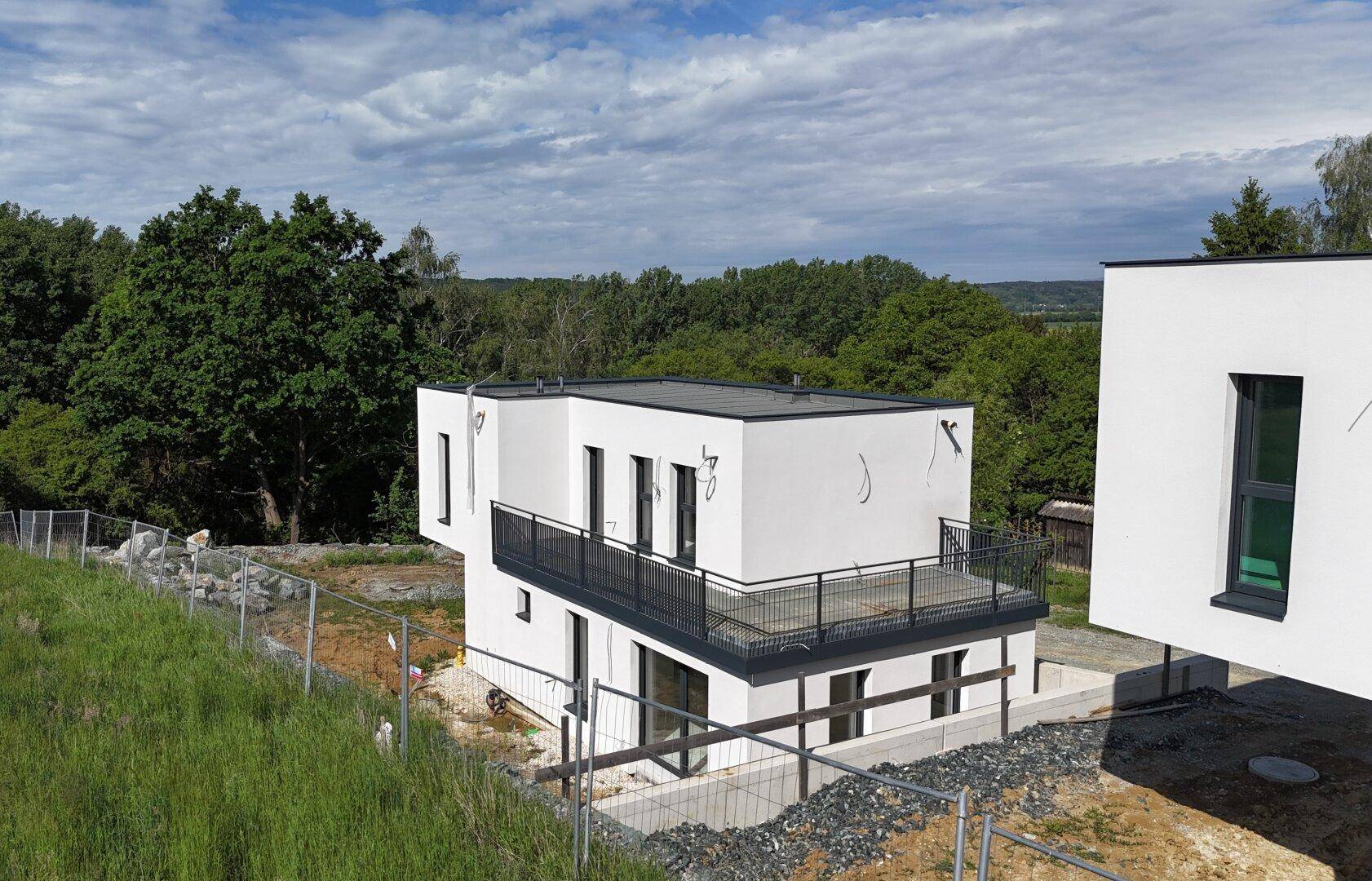 Modernes Einfamilienhaus mit Balkon und Blick auf die umliegende grüne Landschaft.