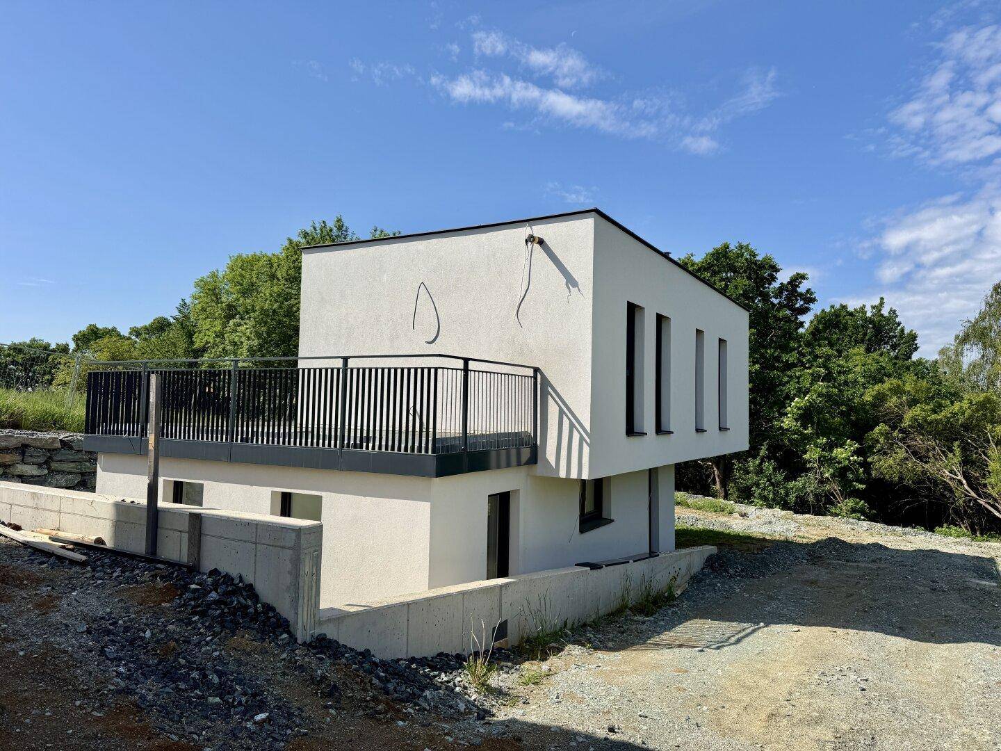 Modernes Einfamilienhaus mit Balkon und minimalistischer Architektur unter strahlend blauem Himmel.