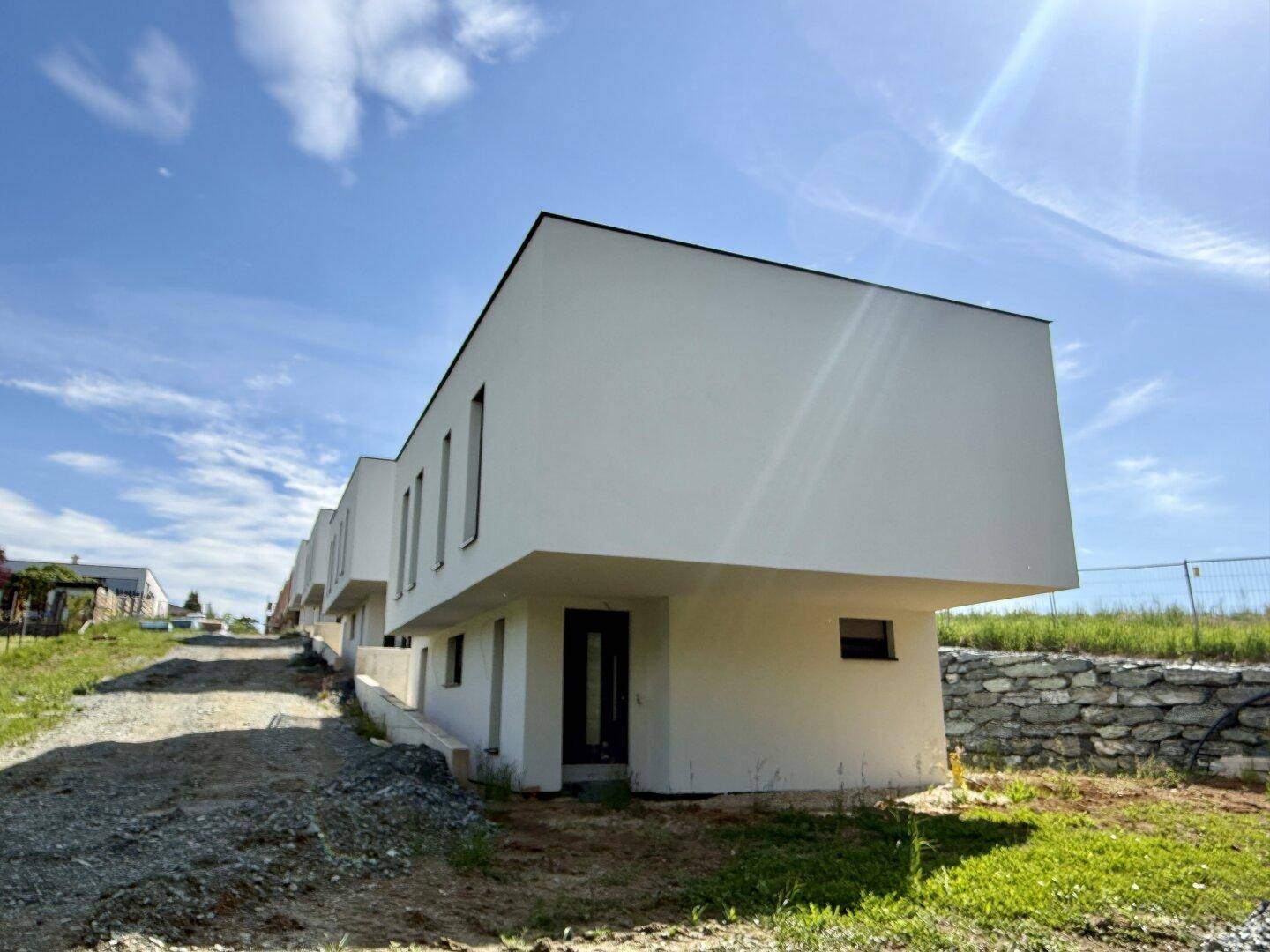 Modernes Einfamilienhaus mit weißer Fassade und minimalistischem Design unter blauem Himmel.