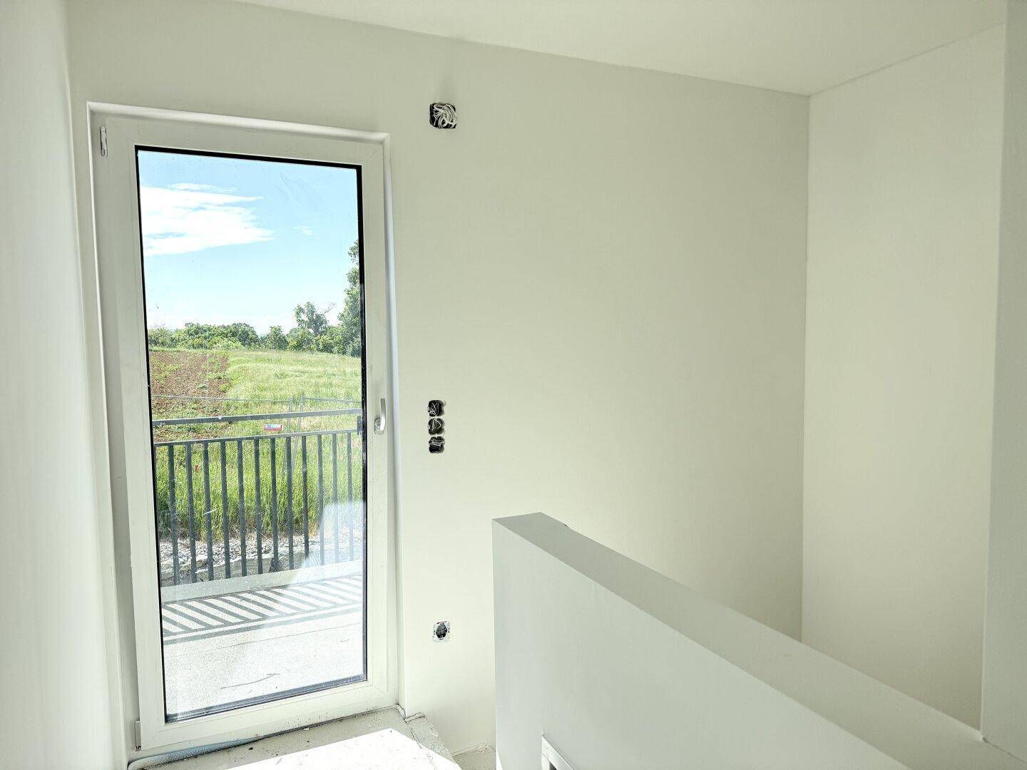 Heller Flurbereich mit Glastür zum Balkon und weitem Blick ins Grüne.