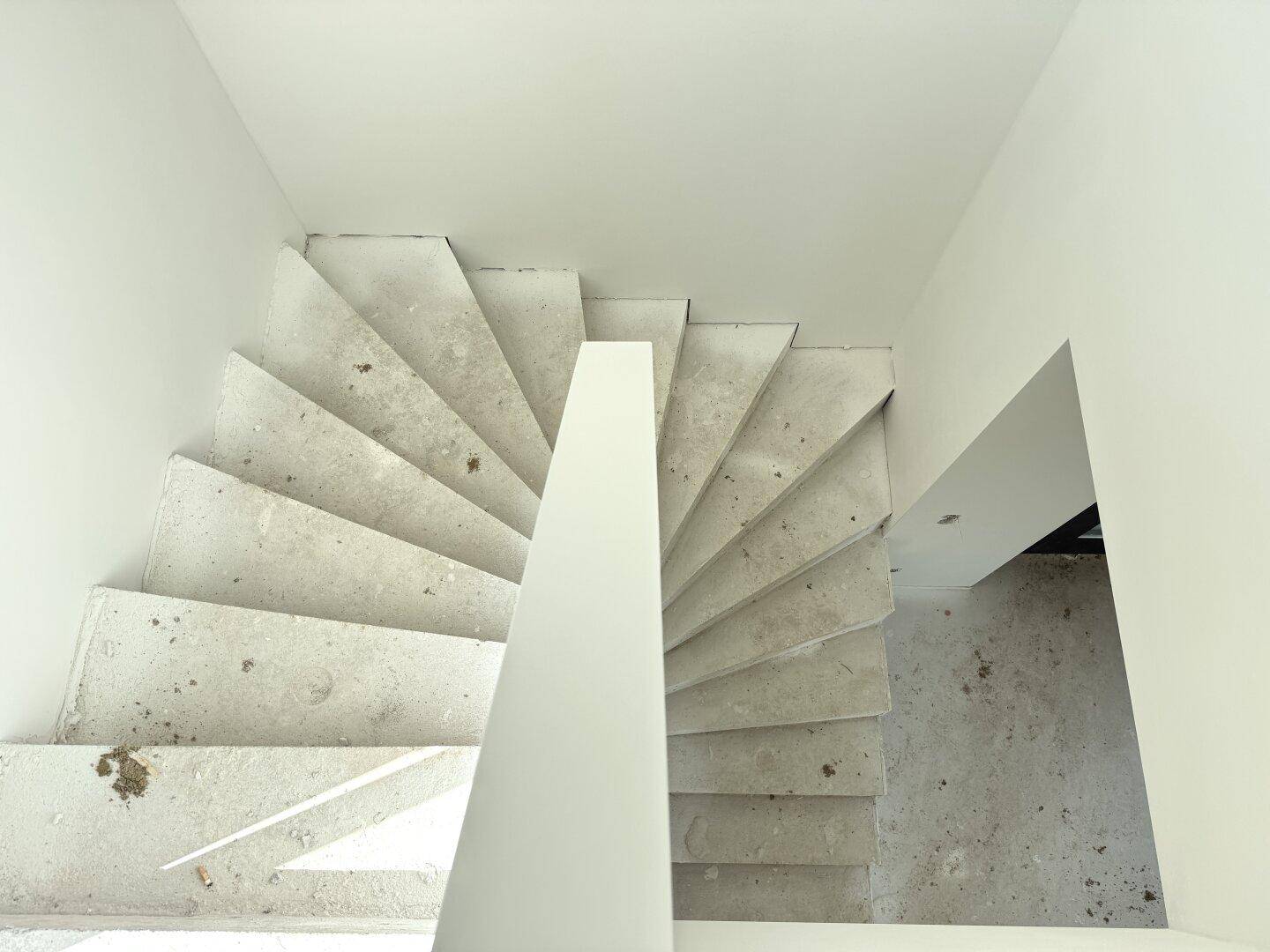 Blick von oben auf eine unfertige Betontreppe mit schlichtem weißem Geländer.