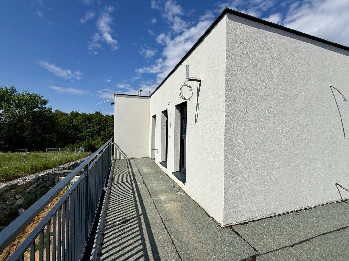 Langer Balkon mit dunklem Geländer an der Seite eines modernen weißen Hauses mit Flachdach.